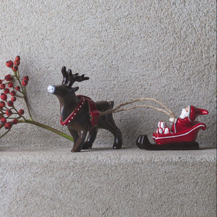 Decorative reindeer pulling a sleigh with Santa Claus on a light gray surface.