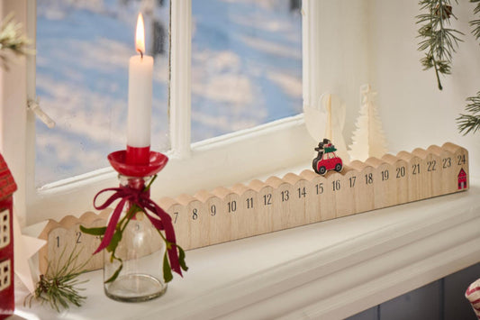 Wooden advent calendar with lit candle and small figures on a windowsill.
