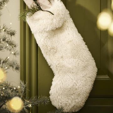 White fluffy Christmas stocking hanging on a green door with festive lights.