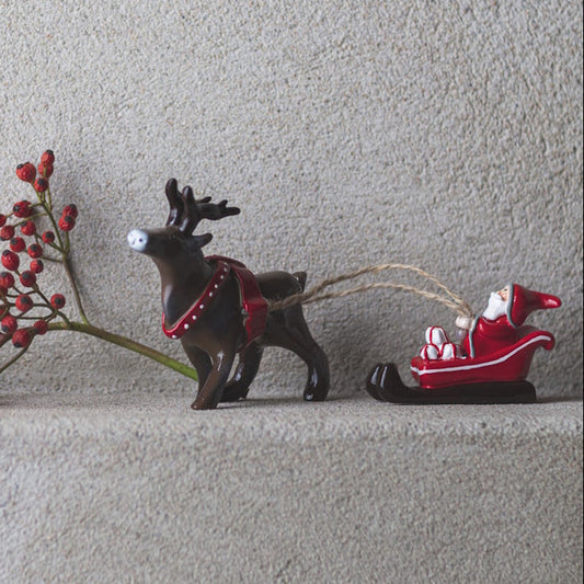 Decorative reindeer pulling a sleigh with Santa Claus on a light gray surface.